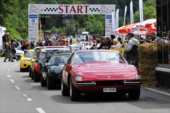 A red sports car at the classic car race prepares at the starting line, surrounded by spectators,