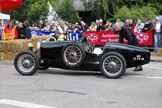 A black historic racing car is pushed by a man at a classic car event, SOLITUDE REVIVAL 2011,