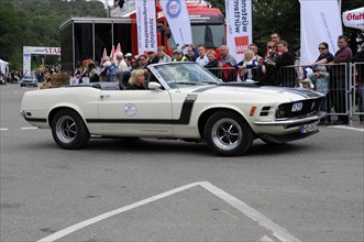 Beige Ford Mustang convertible driving at a classic car event, surrounded by spectators, SOLITUDE