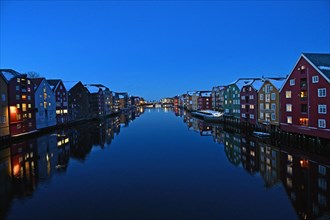 Historic warehouse buildings reflected in the river Nidelva at dusk, Bryggene, Trondheim, Norway,