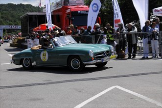 Green Mercedes vintage convertible waiting at the starting line, surrounded by motorsport fans,