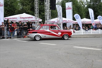 A red and white vintage car drives past enthusiastic spectators on a rally route, SOLITUDE REVIVAL