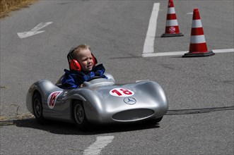 A child in a silver soapbox racing car with the number 18 drives past pylons, SOLITUDE REVIVAL