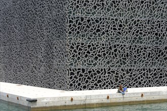 Marseille, Person sitting lonely on the quay wall in front of a wall with extraordinary texture,