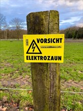 Warning sign on fence post with electric fence from cattle pasture in wolf territory, North