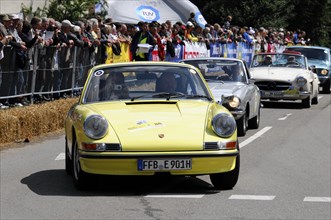 A yellow Porsche 911 classic car takes part in a street race with a view of the crowd, SOLITUDE