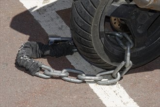 Marseille, A motorbike tyre with a safety chain and a brake disc lock on asphalt, Marseille,