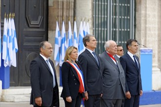 Marseille City Hall, dignitaries stand solemnly at a ceremony with flags in the background,
