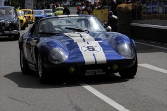 Blue racing car with white stripe and start number driving in front of spectators on a street,