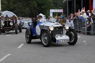 A blue-metallic vintage car drives on a road at a racing event, surrounded by spectators, SOLITUDE
