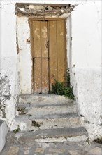 Solabrena, An old, dilapidated door with peeling brown paint, surrounded by a wall and steps,