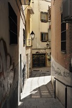 Jaen, Sunny day falls in a narrow, shaded alley with old buildings and a alleyway lamp, Jaen,