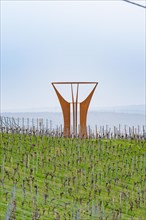 Large metal sculpture in the middle of a vineyard with a hilly landscape in the background, Jesus