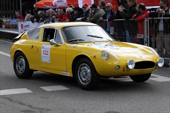 A classic yellow sports car drives past spectators during a road race, SOLITUDE REVIVAL 2011,
