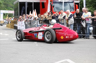 A classic red racing car drives in a street race, watched by spectators during the day, SOLITUDE