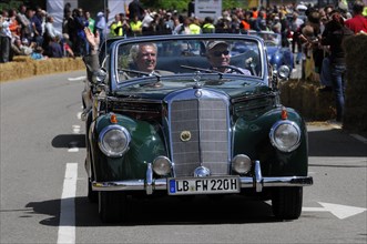 A dark green Mercedes classic car takes part in a parade in front of enthusiastic spectators,