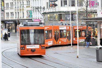 Wuerzburg, Orange tram travelling through an urban street with tracks and passers-by, Wuerzburg,