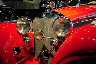 Front view of a red classic car with shiny headlights and chrome accents, Mercedes-Benz Museum,