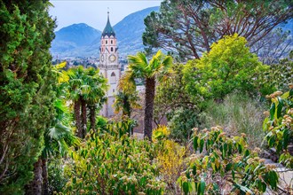 Subtropical vegetation in spring on the Tappeiner promenade with the tower of the parish church,