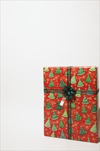 Close-up of box shaped Christmas gift wrapped with red and green wrapping paper on white