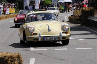 A yellow vintage sports car takes part in a street race, surrounded by spectators, SOLITUDE REVIVAL