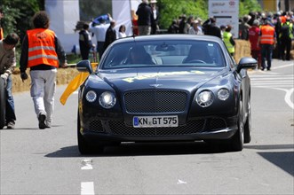 A dark blue Bentley drives on a street at an event in the sunshine, SOLITUDE REVIVAL 2011,