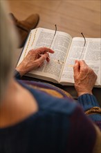 An elderly person sitting and reading a book, holding the glasses in his hands, Bible Circle, Jesus