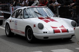 A white Porsche racing car with racing stripes takes part in a car race, spectators in the