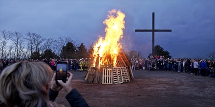 A woman photographs the Easter bonfire on the Haniel spoil tip in front of the summit cross,