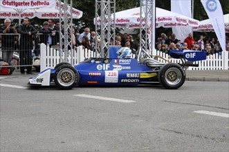 Blue and yellow formula racing car drives in front of spectators at the race track, SOLITUDE