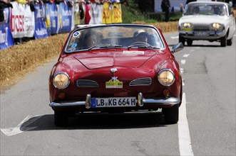 A red vintage sports car drives along in front of spectators during a street race, SOLITUDE REVIVAL