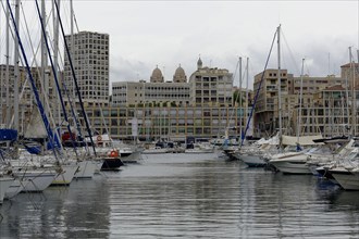 Marseille harbour, sailboats in the harbour with cloudy sky and urban scenery in the background,