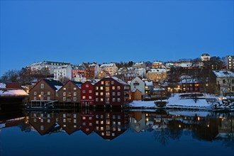 Historic warehouse buildings reflected in the river Nidelva at dusk, Bryggene, Trondheim, Norway,