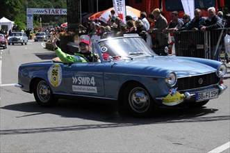 A blue open-top vintage rally car with a smiling driver in front of spectators, SOLITUDE REVIVAL