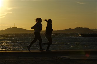 Marseille in the evening, Two joggers run along the sea at sunset, their silhouettes stand out,