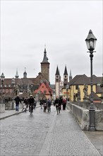 Wuerzburg, Busy pedestrians on a bridge with historic buildings and a tower in the background,