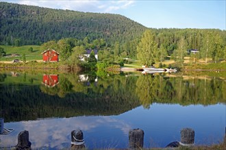Trees, houses and a small boat are reflected in a calm lake, old waterway, Telemark Canal,