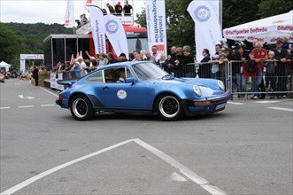 A blue classic car drives past a race while spectators watch, SOLITUDE REVIVAL 2011, Stuttgart,