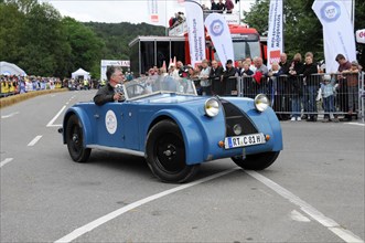 A blue vintage car drives past a street race with smiling spectators, SOLITUDE REVIVAL 2011,