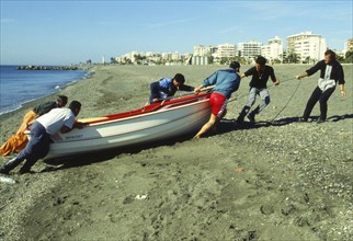 Fisherman pulling up boat on the beach in Torre del Mar, Malaga province, Costa del Sol, Andalusia,