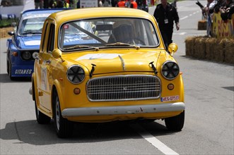 Yellow damaged vintage car with racing number and recognisable racing environment and spectators,