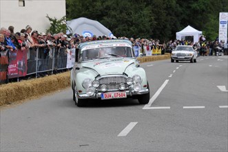 A white vintage racing car drives past spectators and hay bales on a road rally, SOLITUDE REVIVAL