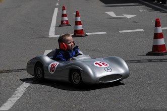 Smiling child enjoying a ride in a silver soapbox on a closed-off road, SOLITUDE REVIVAL 2011,