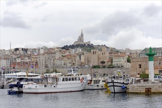 Marseille, view of a harbour with boats and the city in the background under a cloudy sky,