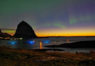Northern lights (aurora borealis) mingle with sunset, sea, striking mountains and fish farm,