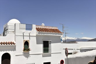 Solabrena, Traditional white building with tiled roof and round arch in front of the Sierra Nevada,