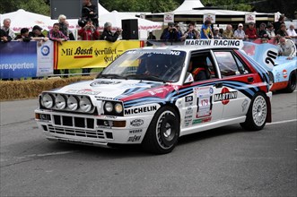 A Lancia rally car with Martini Racing stickers drives past spectators on a road, SOLITUDE REVIVAL