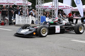 Black racing car with gold-coloured details on a race track, audience in the background, SOLITUDE