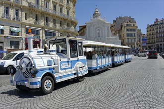 Marseille, A blue and white tourist train passes in front of a church with passengers on board,