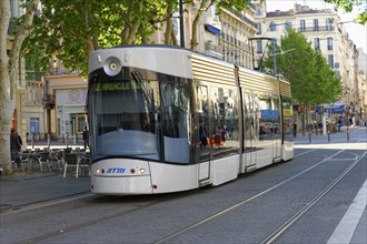Tram travelling through an urban scene with trees and buildings, Marseille, Departement